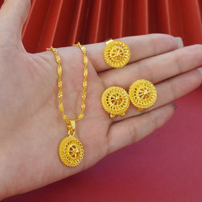 Gold-plated three-piece jewellery set showing necklace with floral pendant, matching earrings, and ring on a grey background.