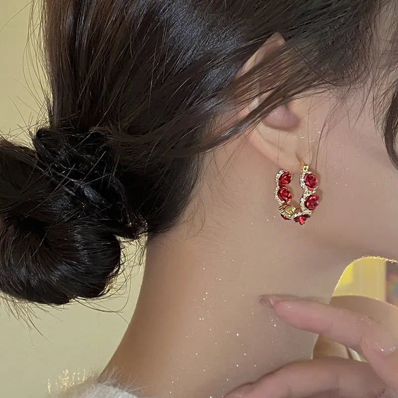 A pair of red rose-shaped clip-on alloy earrings for women on a white background.