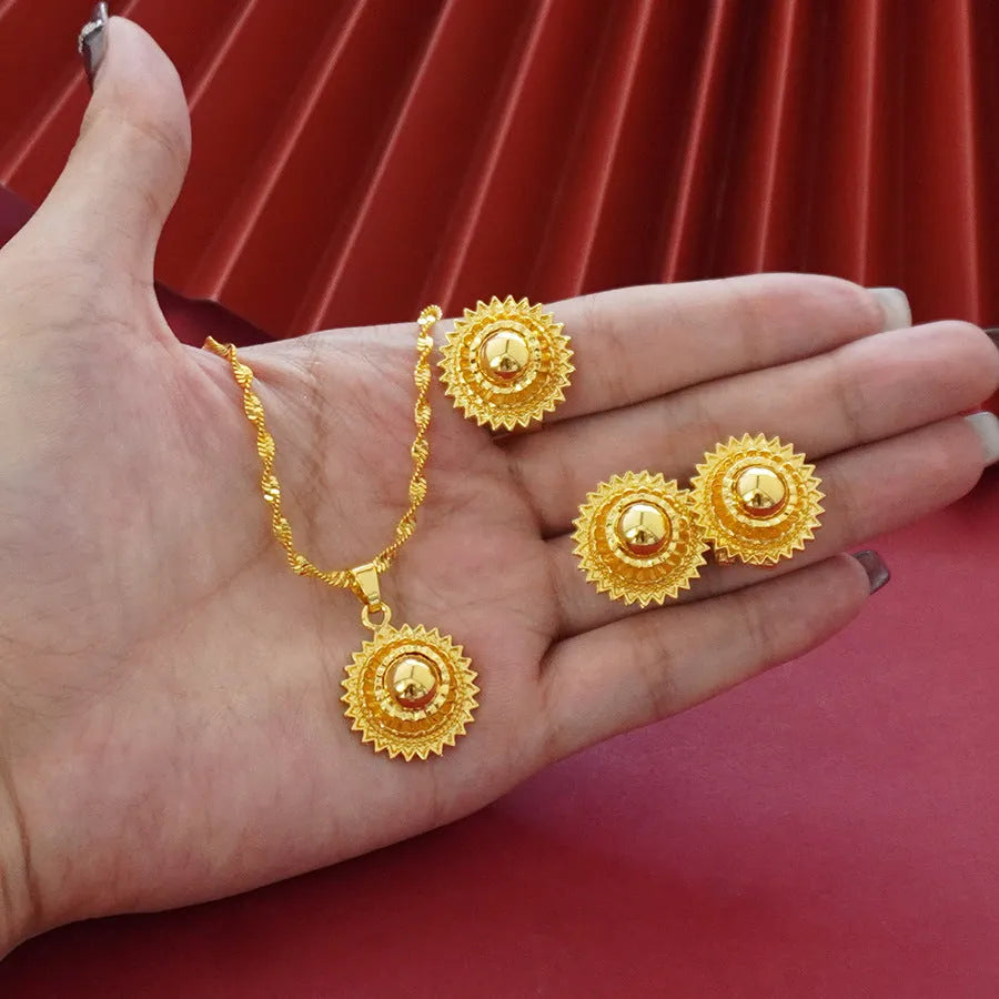 Gold-plated three-piece jewellery set showing necklace with floral pendant, matching earrings, and ring on a grey background.