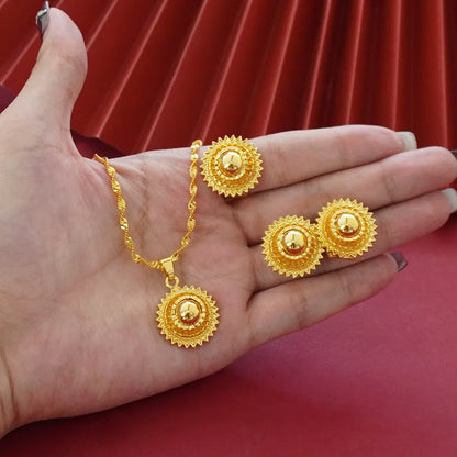 Gold-plated three-piece jewellery set showing necklace with floral pendant, matching earrings, and ring on a grey background.