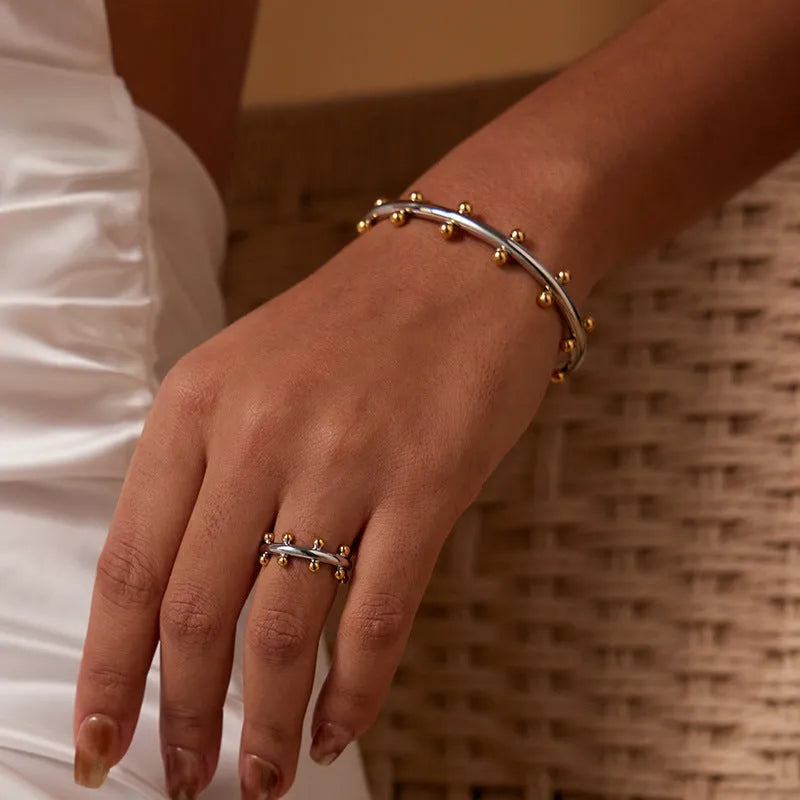 Close-up of a textured stainless steel C-shaped bracelet with rivet-shaped bean beads in a gold finish.