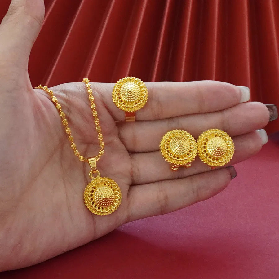 Gold-plated three-piece jewellery set showing necklace with floral pendant, matching earrings, and ring on a grey background.