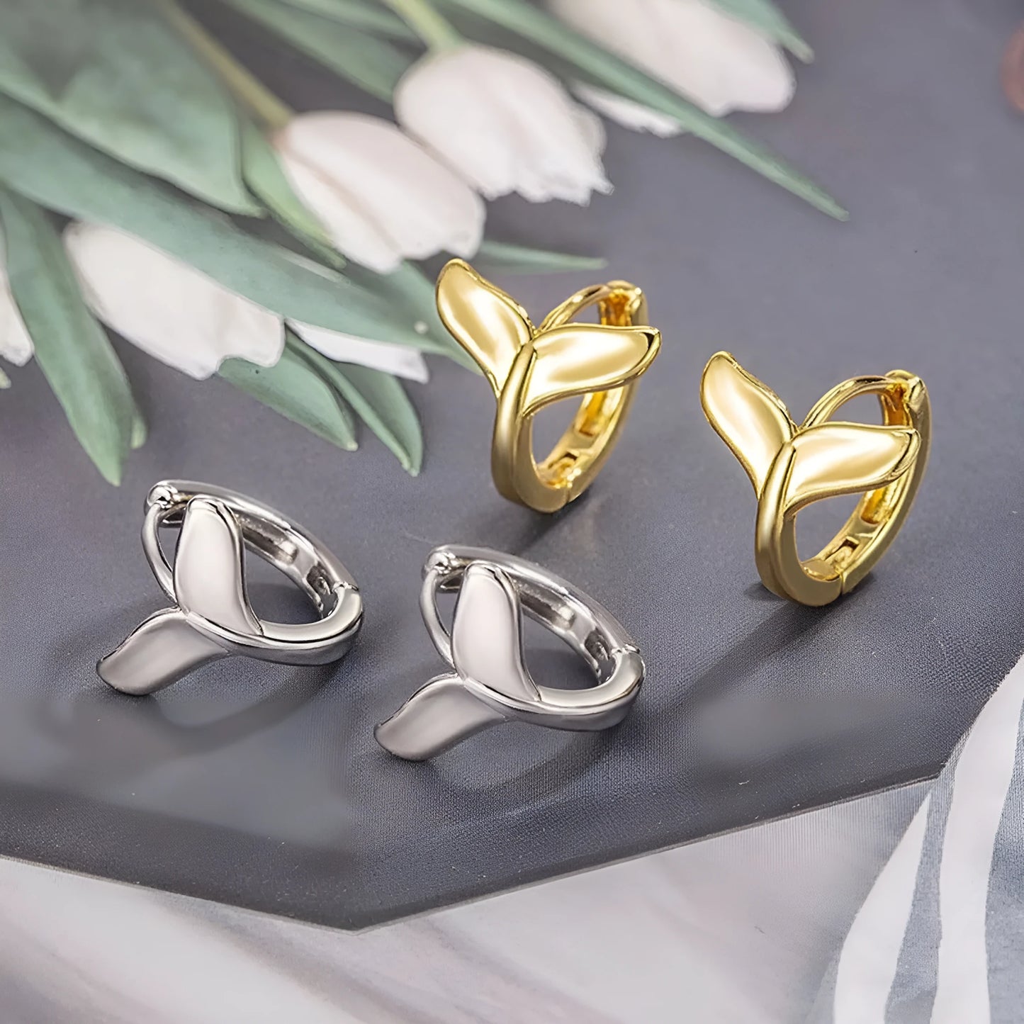 A pair of simple fishtail design earrings with an electroplated metallic finish, shown in white gold and yellow gold colour options.