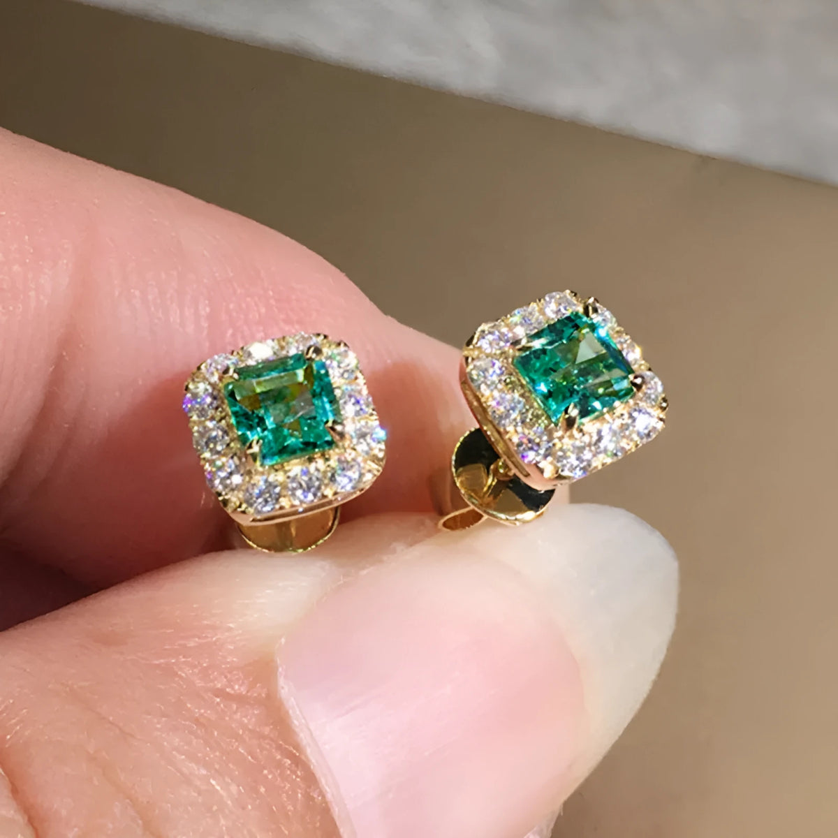 A pair of square cut grandmother green zircon stud earrings with a gold electroplated finish on a white background.