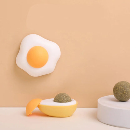 Fried egg shaped plush cat toy stuck to a window with a cat paw batting the 360-degree rotating ball.