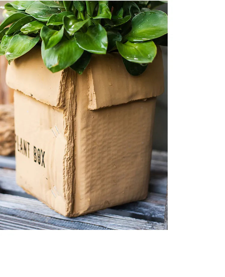 A grey cement flowerpot with a folded paper box design, shown with a drainage hole in its base.