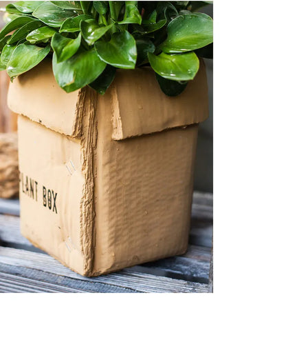 A grey cement flowerpot with a folded paper box design, shown with a drainage hole in its base.