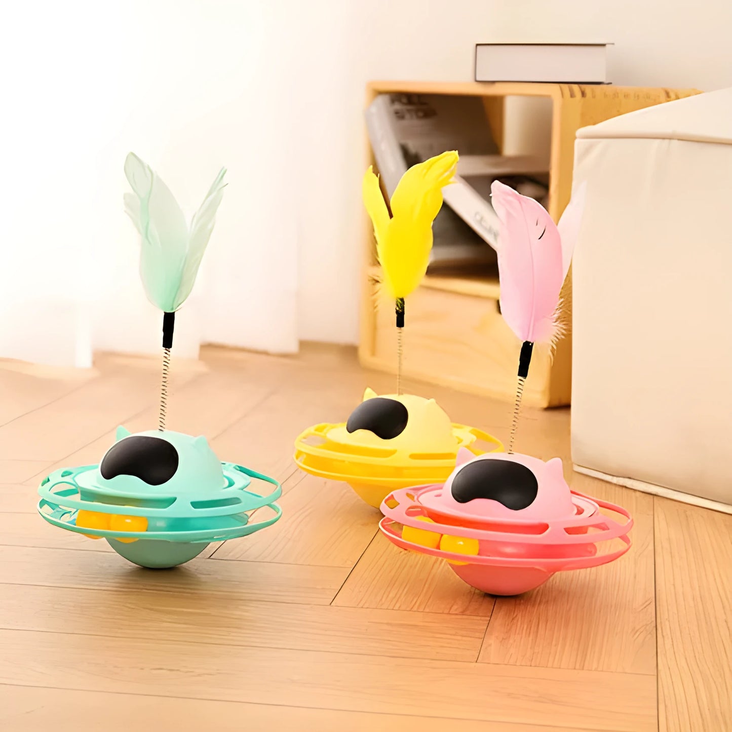 Pink self-hi tumbler cat toy with plush element on a turntable base, next to a play stick.
