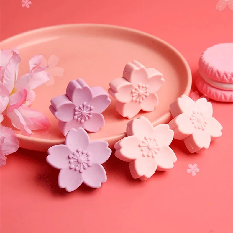 Assorted colourful cherry blossom shaped student erasers on a white background.