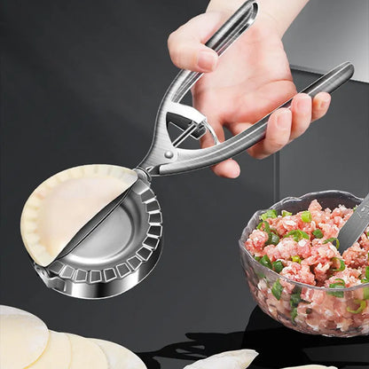 Silver stainless steel manual dumpling press with hinged handles on a wooden kitchen surface.
