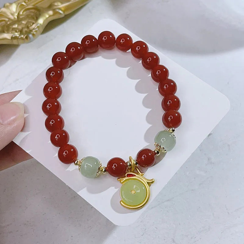 Close-up of a red agate bracelet with a dragon charm and Lucky Bag symbol on a wrist.