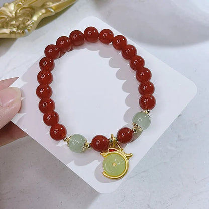 Close-up of a red agate bracelet with a dragon charm and Lucky Bag symbol on a wrist.