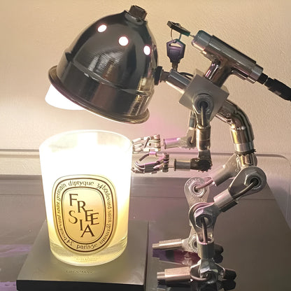Silver copper robot-shaped decorative desk lamp with custom graphic option on a wooden shelf.