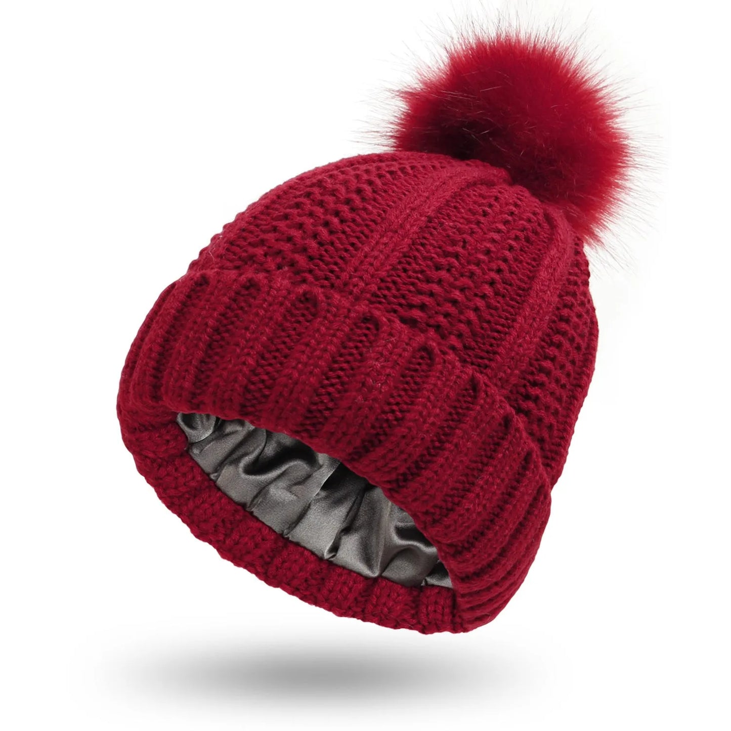 Woman wearing a wine red wool beanie hat with a faux fur pom pom and satin lining.