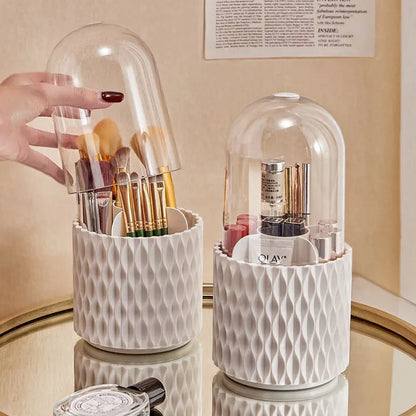 White rotating acrylic makeup brush holder with transparent dustproof lid on a desktop.
