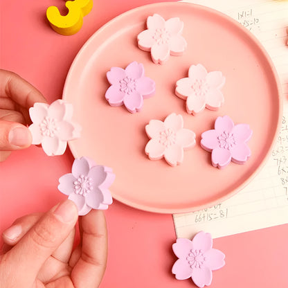 Assorted colourful cherry blossom shaped student erasers on a white background.