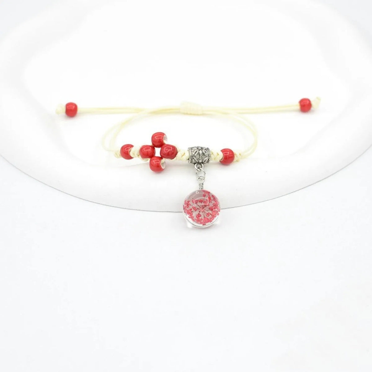 Close-up of a hand-woven bracelet with a large 1.4cm glass bead containing colourful dried flowers.