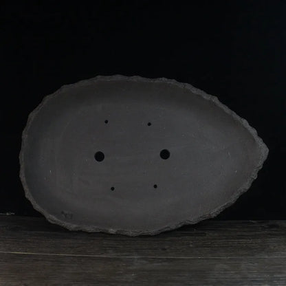 Handmade purple clay flower pot in a creative shape on a floor.