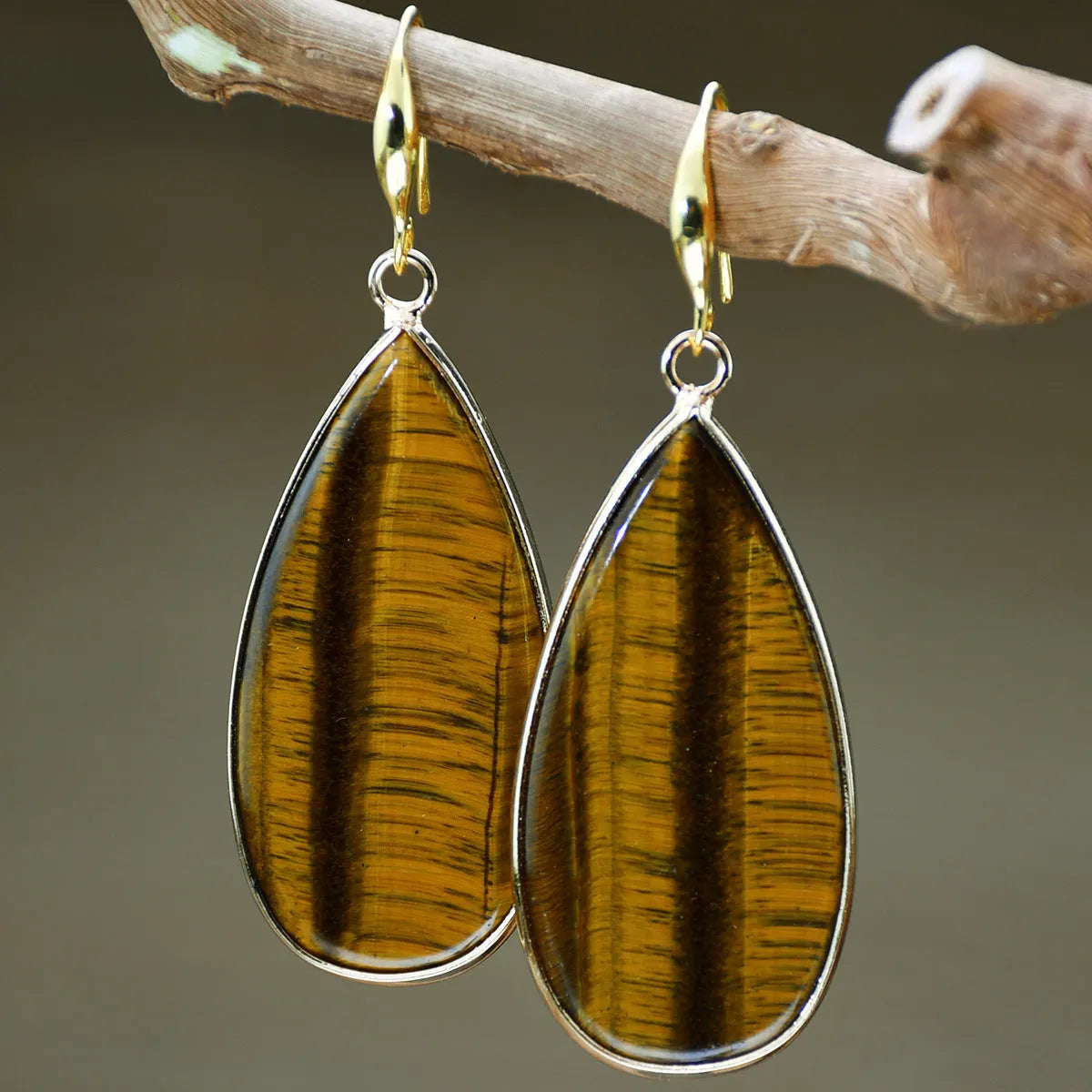 Handmade vintage long water drop earrings with tigereye stone and sterling silver hooks on a textured background.