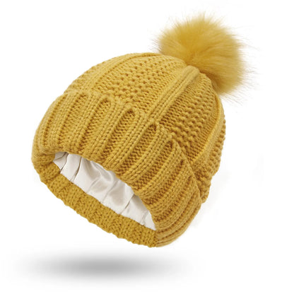 Woman wearing a wine red wool beanie hat with a faux fur pom pom and satin lining.