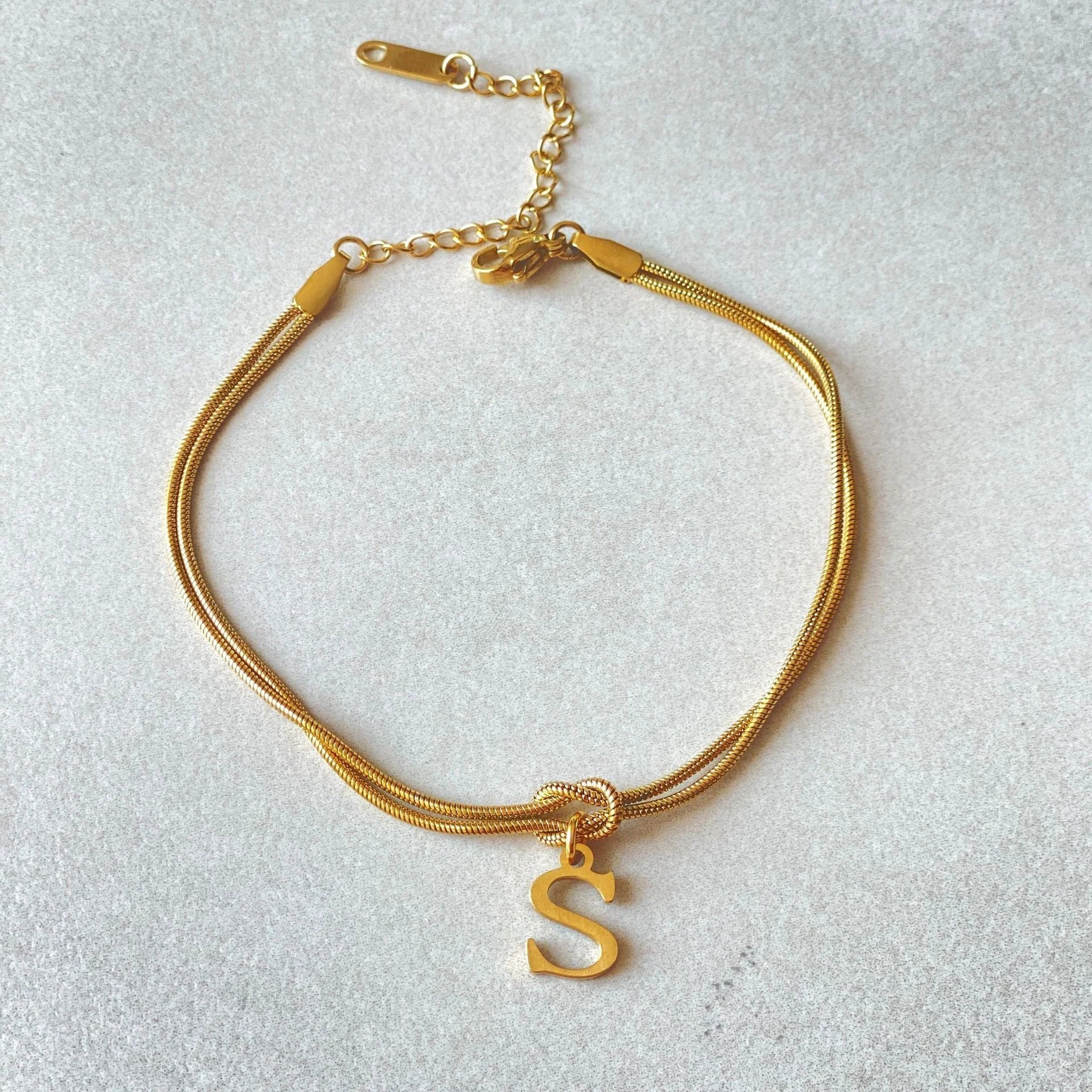 Elegant letter charm bracelets for women in gold and silver tones, featuring a delicate snake chain design and personalised letter charms.