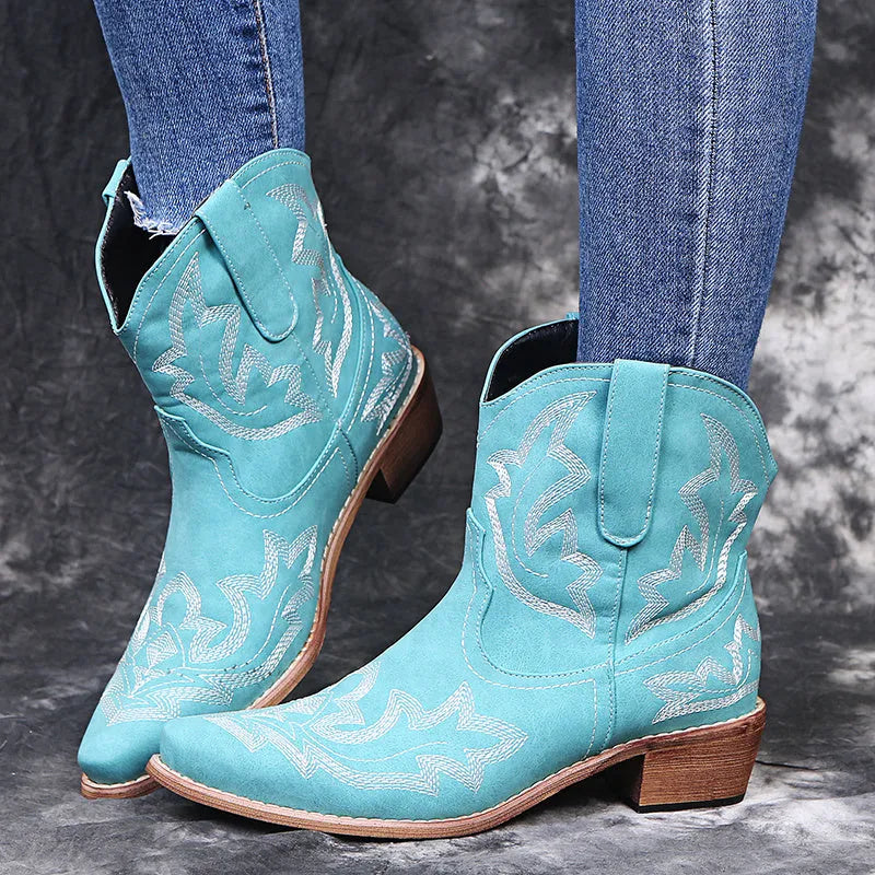 Blue women's cowboy ankle boots with embroidery and a low wedge heel on a wooden floor.