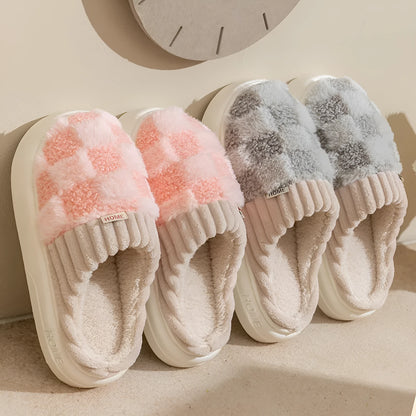Plaid pattern women's plush slippers with coral velvet upper and textured PVC sole on a wooden floor.