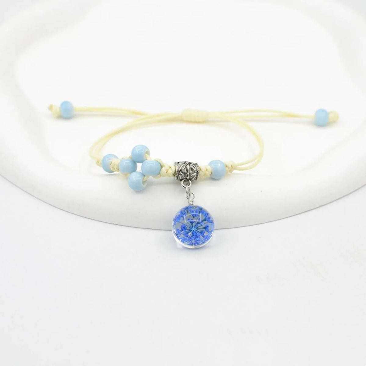 Close-up of a hand-woven bracelet with a large 1.4cm glass bead containing colourful dried flowers.