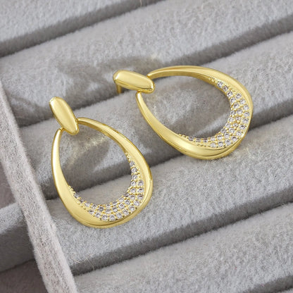 Women's yellow gold geometric drop earrings with oval and round elements on a white background.