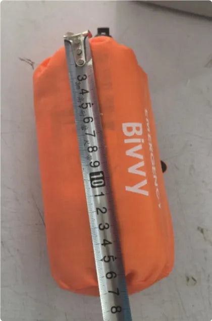 Orange emergency tent with sleeping bag and blanket disaster relief kit on ground