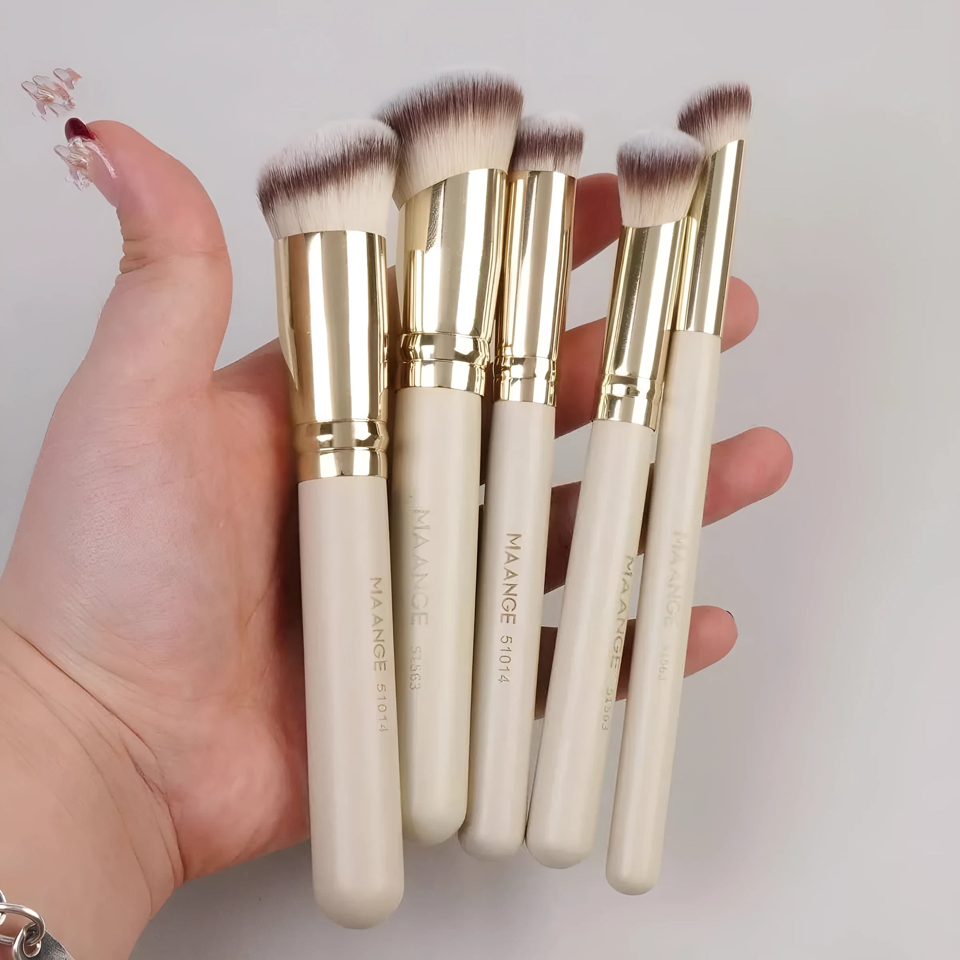 Apricot-coloured angled blush brush and four other synthetic makeup brushes on a white background