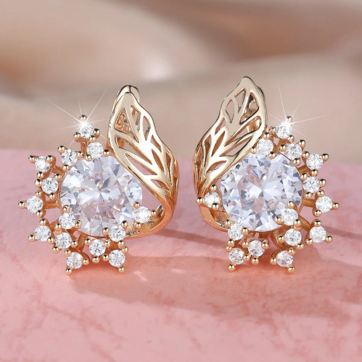 Rose gold plated women's stud earrings with a round flower shape, feather detail, and a central cubic zirconia stone.