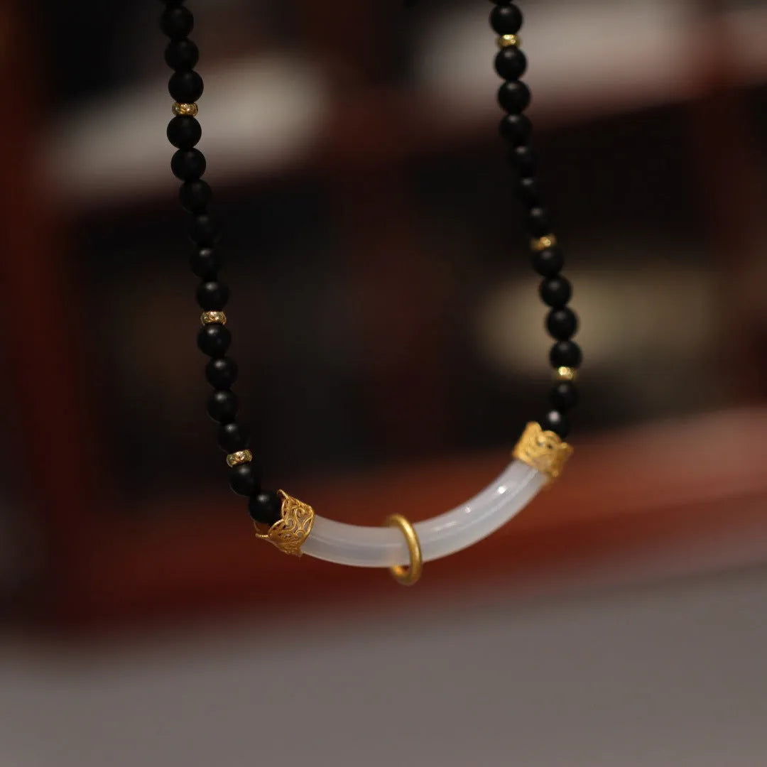 Close-up of a U-shaped necklace with frosted black agate, white chalcedony, and a 925 silver pendant on a beaded chain.