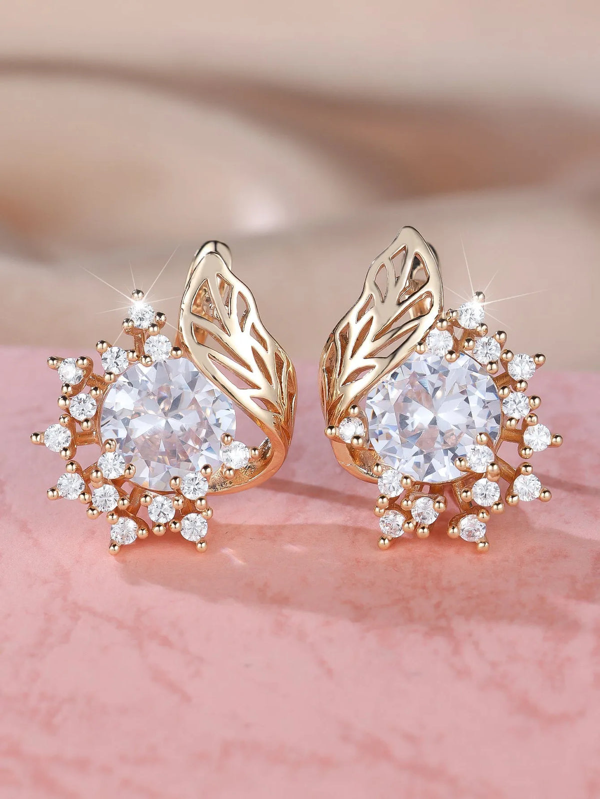 Rose gold plated women's stud earrings with a round flower shape, feather detail, and a central cubic zirconia stone.