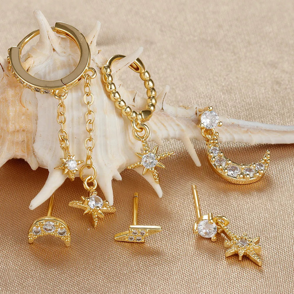 Set of six gold-coloured XINGX chain tassel stud earrings with zircon details on a flat surface.