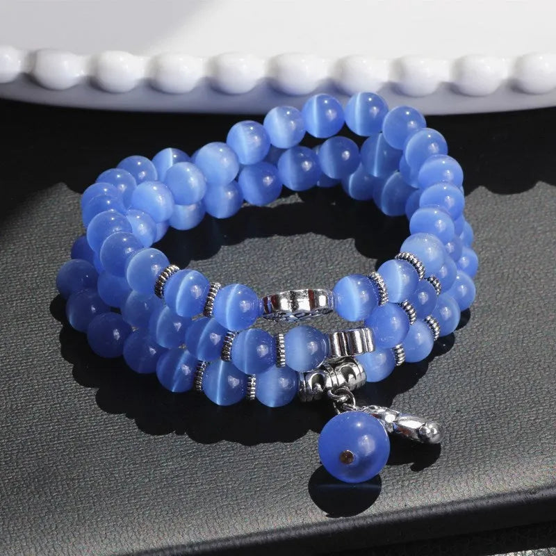 Close-up of a women's opal cat eye bracelet with three geometric rings and a lucky cat charm on a long, adjustable cord.