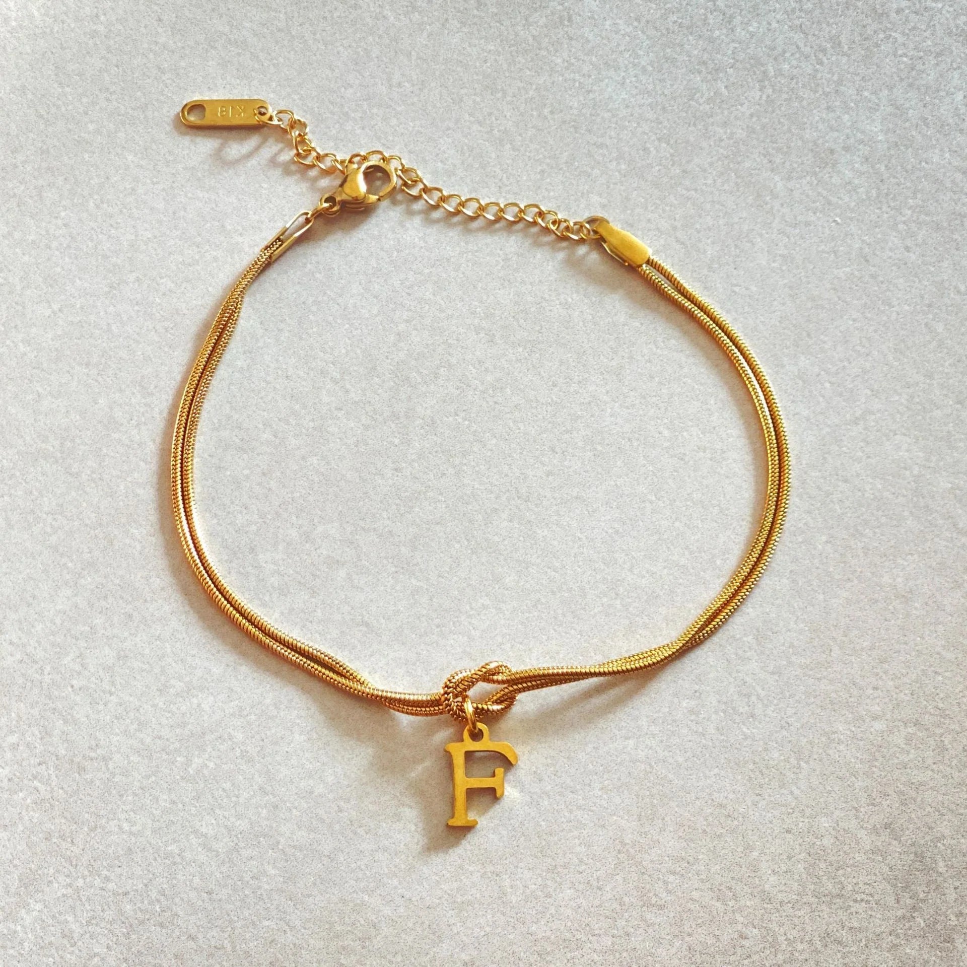 Elegant letter charm bracelets for women in gold and silver tones, featuring a delicate snake chain design and personalised letter charms.