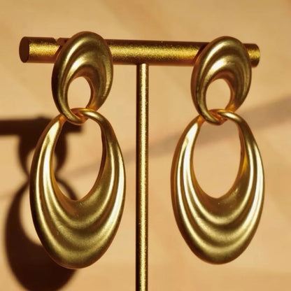 A pair of gold-coloured U-shaped women's earrings with a double circle design on a plain background.