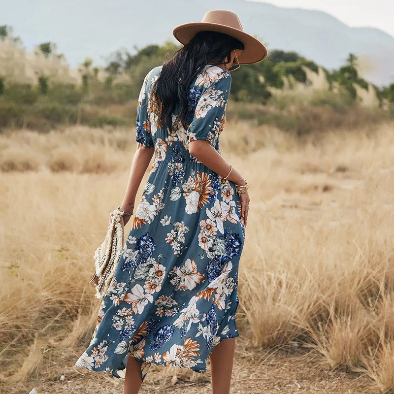 Floral summer beach dress with V-neck and elastic waist in mid-length large hemline design, available in black, blue and yellow colours, with regular short sleeves and high waist styling for women in S, M, L, XL, and XXL sizes