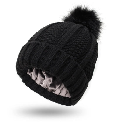 Woman wearing a wine red wool beanie hat with a faux fur pom pom and satin lining.