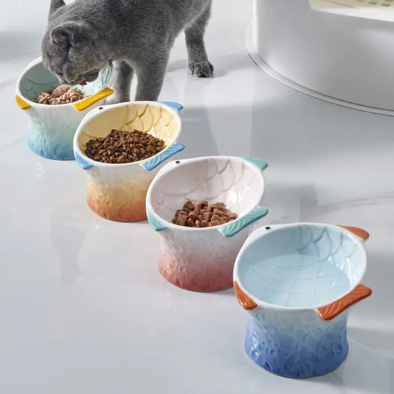 Set of four blue fish-shaped ceramic cat bowls with a tilted design on a wooden floor.