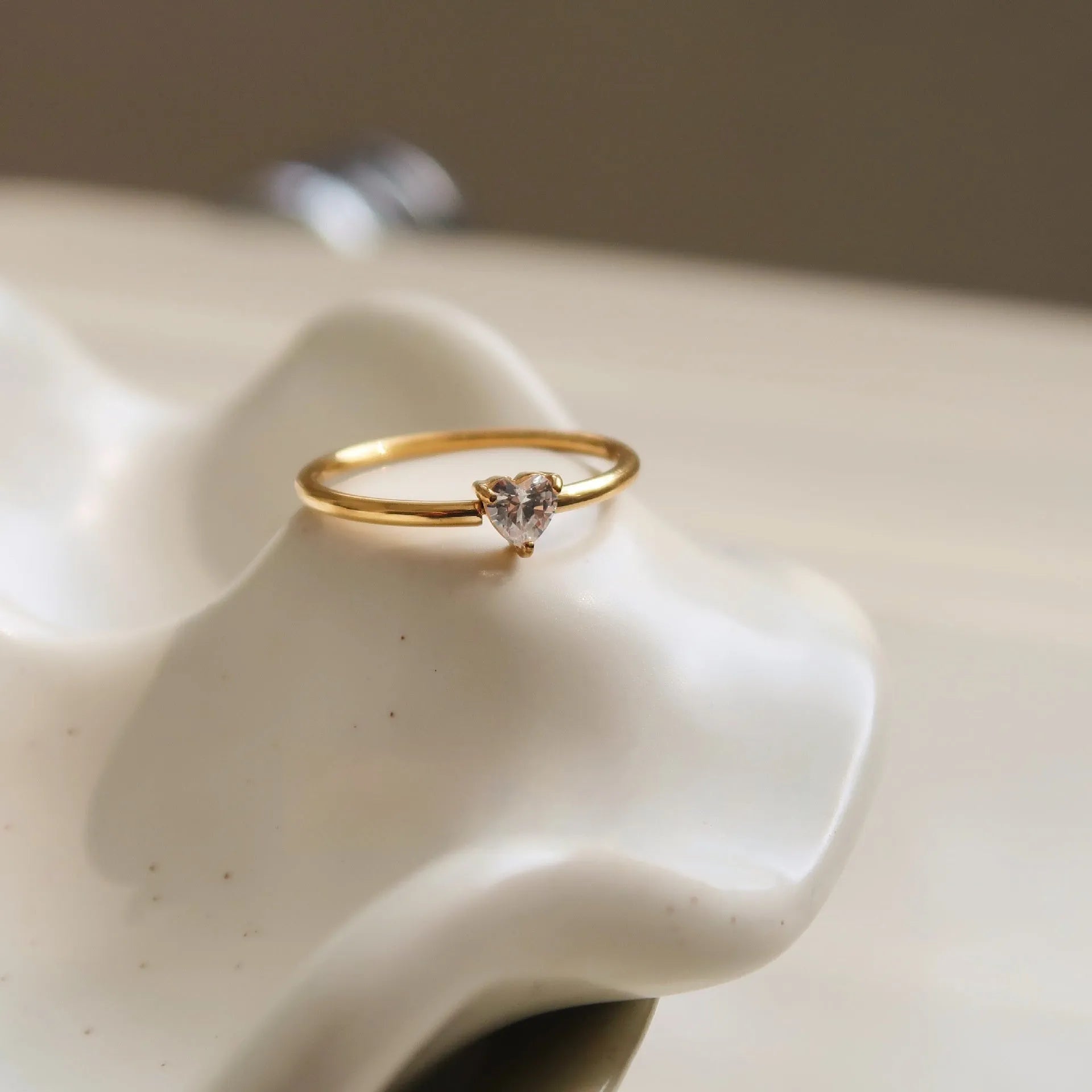 A gold-coloured stainless steel ring in a heart shape and an oval shape on a simple band.