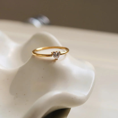 A gold-coloured stainless steel ring in a heart shape and an oval shape on a simple band.