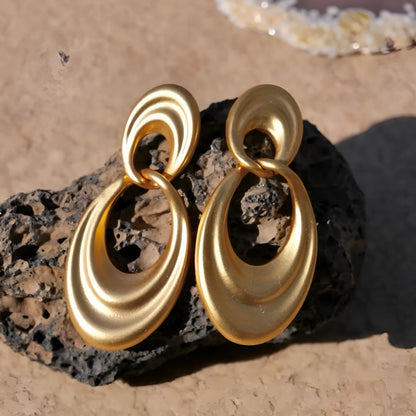 A pair of gold-coloured U-shaped women's earrings with a double circle design on a plain background.