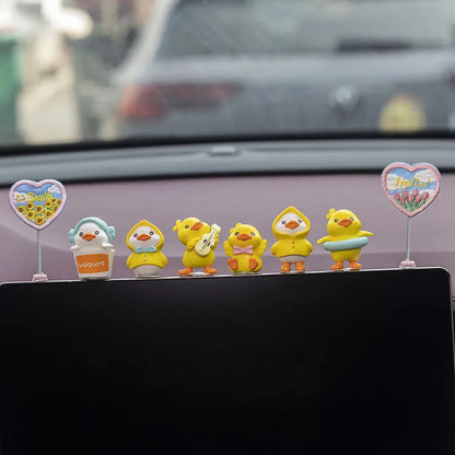 Set of six small yellow PVC duckling car decorations and one cartoon sign on a car dashboard.