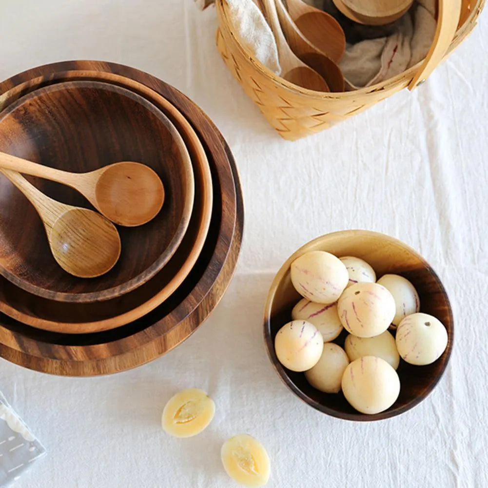 Set of five brown wooden bowls in different sizes on a wooden table, showing natural grain.
