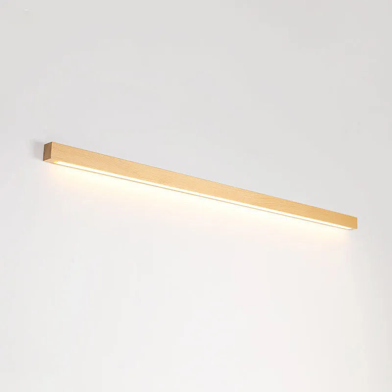 Slim walnut-coloured wooden strip wall lamp with acrylic light diffuser mounted on a plain wall.