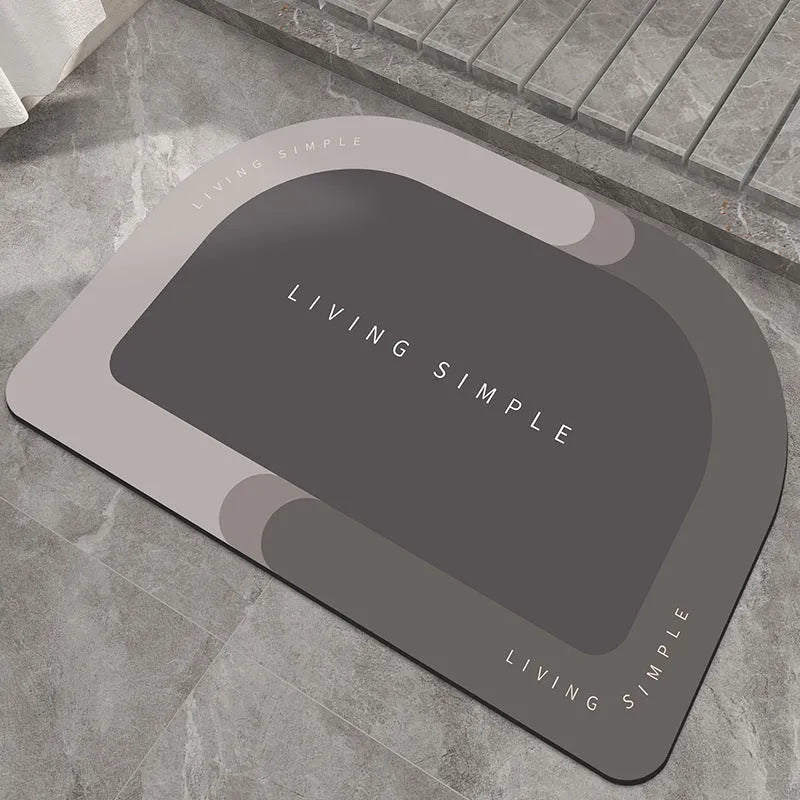 Oval grey bath mat with non-slip rubber bottom on a tiled floor, showing absorbent fabric surface
