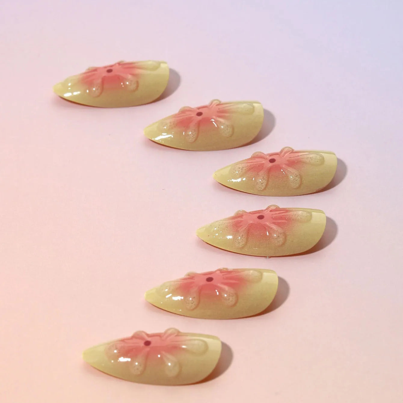 Set of simple fake nails with cartoon 3D flower design, jelly glue pot, and a nail file on a table.
