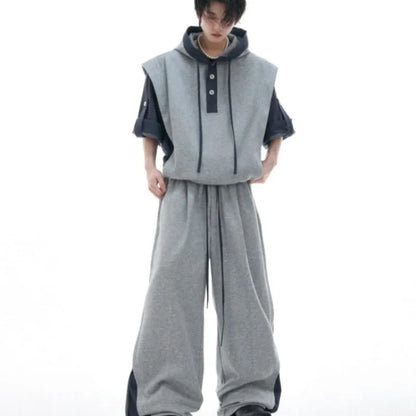 Man wearing a grey hooded short-sleeve tracksuit jacket with black trousers, showing three-dimensional stitching detail.